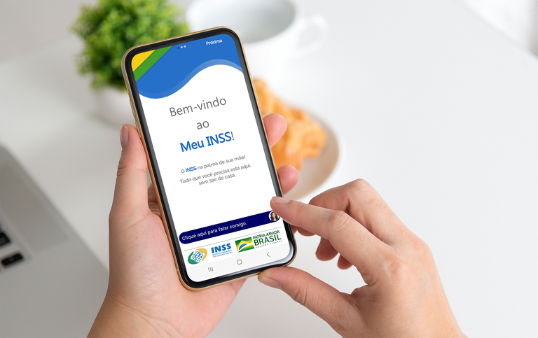  Pessoa acessando o aplicativo Meu INSS no celular, representando os canais de atendimento digital do INSS.