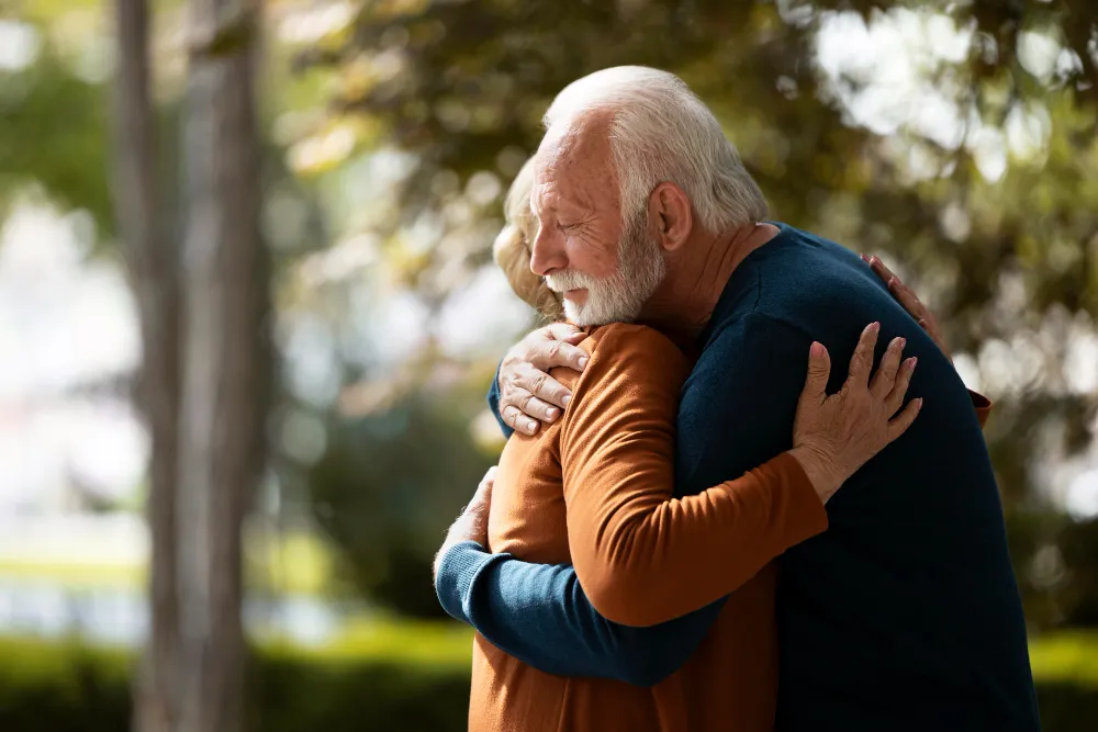 Dois idosos se abraçando com emoção em um ambiente ao ar livre.