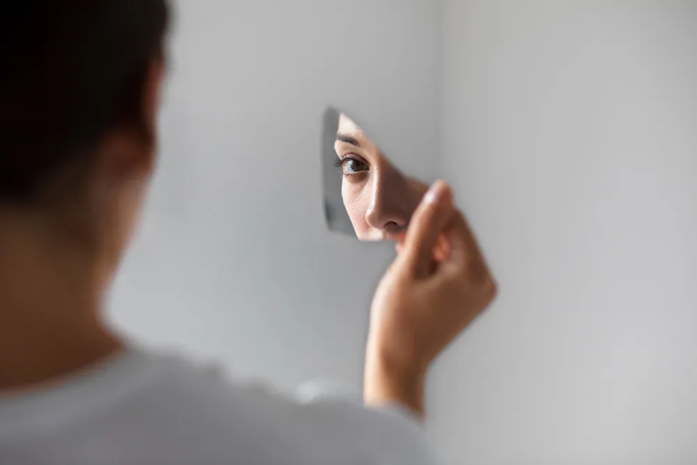 Reflexo de uma mulher em um espelho quebrado, representando aceitação da imperfeição.