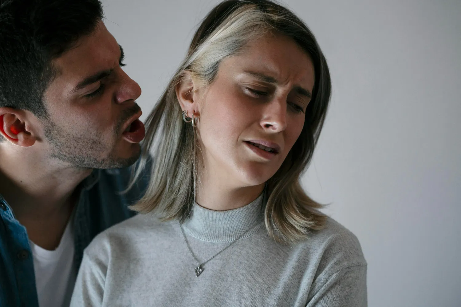 Homem gritando perto do rosto de uma mulher angustiada, que desvia o olhar com expressão de medo.