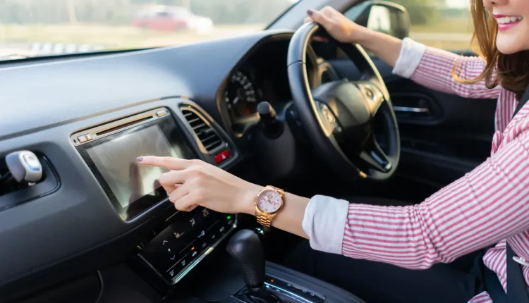 Pessoa tocando na tela sensível do painel de um carro enquanto dirige.