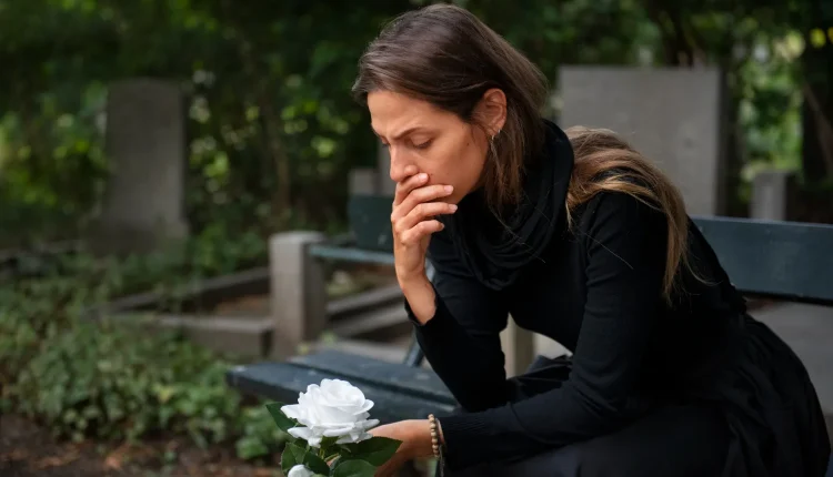 Mulher em luto segurando uma rosa branca em um cemitério, refletindo sobre a perda