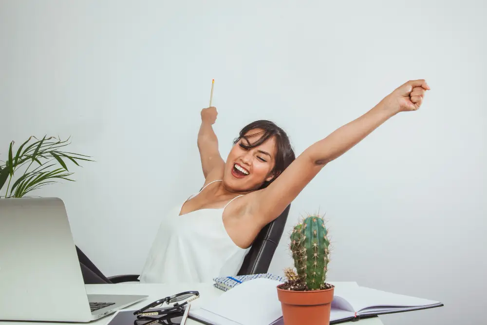 Pessoa levantando os braços com expressão de felicidade, simbolizando a motivação interna e busca por excelência no trabalho.