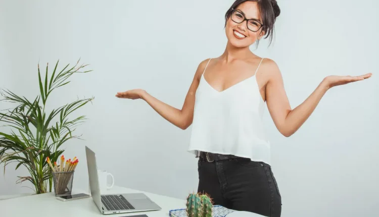 Mulher sorridente em um ambiente de trabalho com um laptop e um cacto sobre a mesa.