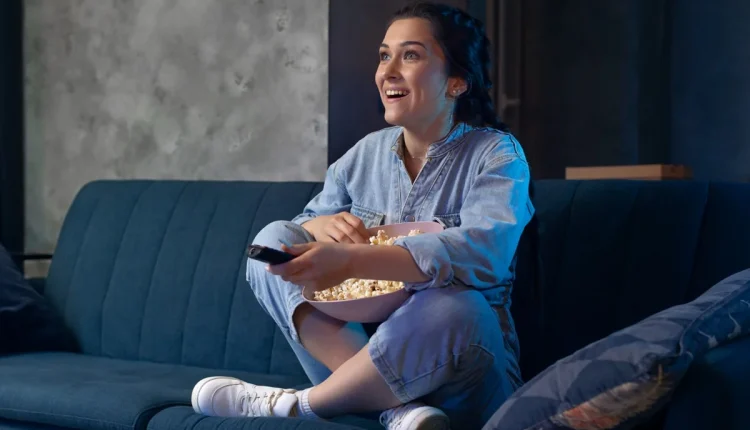 "Mulher assistindo TV e comendo pipoca, refletindo sobre o impacto da televisão na solidão.