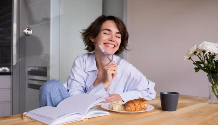 Mulher sorrindo enquanto toma café e escreve em um caderno, representando a prática de rituais matinais para o sucesso.