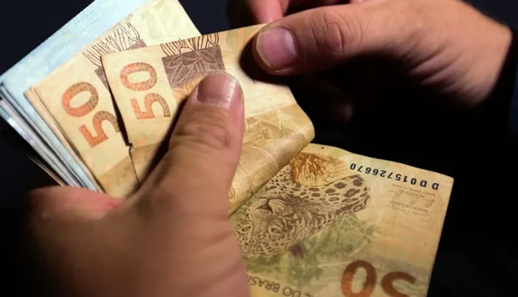 Pessoa contando cédulas de 50 reais, representando o pagamento do salário mínimo.