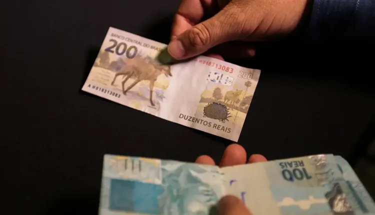 Pessoa segurando uma cédula de R$ 200 e uma de R$ 100, ilustrando o valor do pagamento do Pix de R$ 2.800