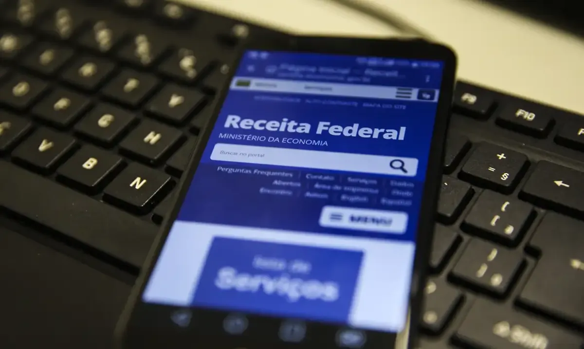 Smartphone exibindo a página da Receita Federal com a opção de consulta para a restituição do Imposto de Renda (IR), simbolizando o uso do aplicativo para acompanhar o lote residual.